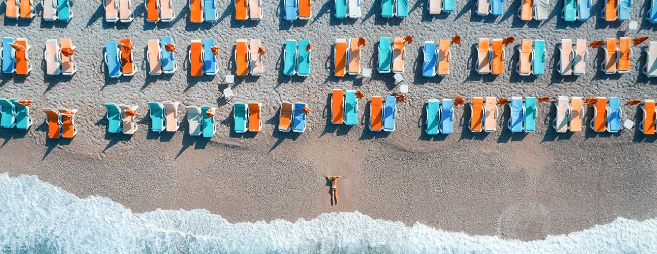 Aerial view of lying woman on the beach Beautiful young woman on the sea at sunrise in Oludeniz, Turkey. Aerial view of lying woman on the beach with colorful chaise-lounges. Top view from drone. Seascape with girl, azure water and waves
