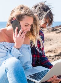 Happy modern beautiful couple enjoying technology outdoor togeth Happy modern beautiful couple enjoying technology outdoor together in friendship or relationship - young people with laptop and phone internert connected - ocean in background